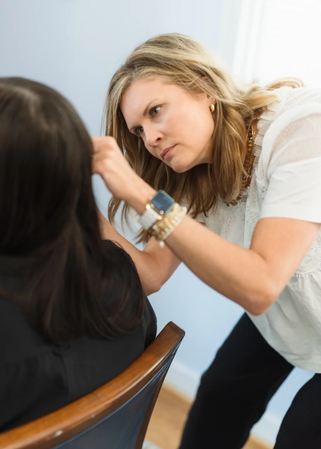 Headshots and branding for Davis Audiology in Taylors SC.: A hairstylist leans toward a seated client, carefully working on the client&rsquo;s dark hair in a salon.