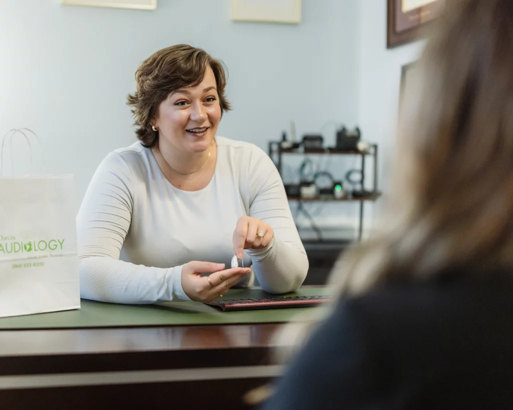 Headshots and branding for Davis Audiology in Taylors SC.: Audiologist smiling and demonstrating a small hearing device to a client across a desk.