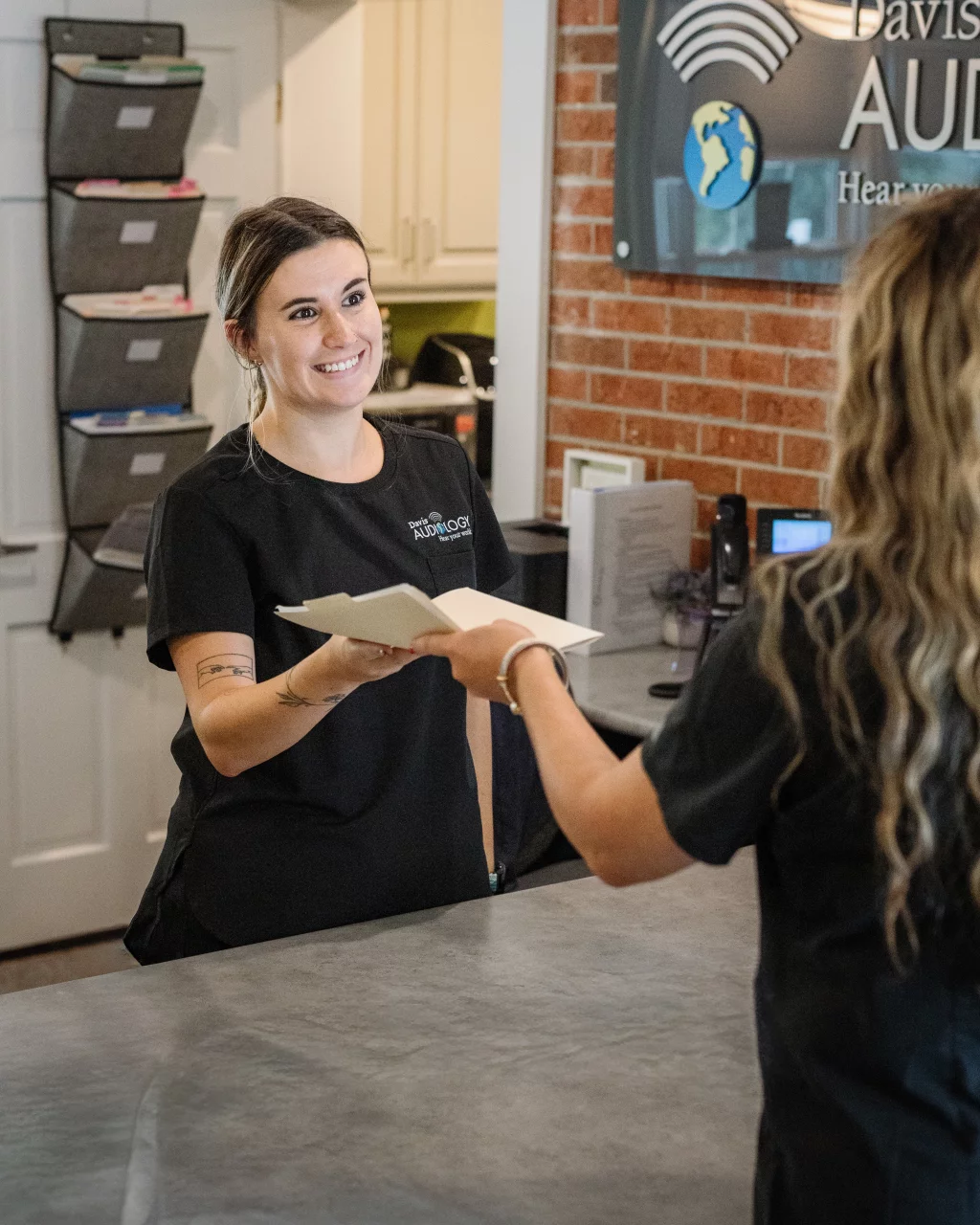Headshots and branding for Davis Audiology in Taylors SC.: Audiology clinic receptionist smiling and handing paperwork across the front desk to a client.