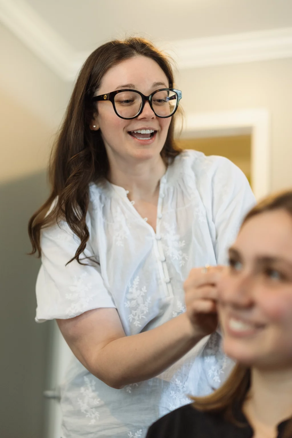 Headshots and branding for Davis Audiology in Taylors SC.: Smiling woman in glasses and a white blouse reaches toward another woman in the foreground, who is smiling and out of focus.