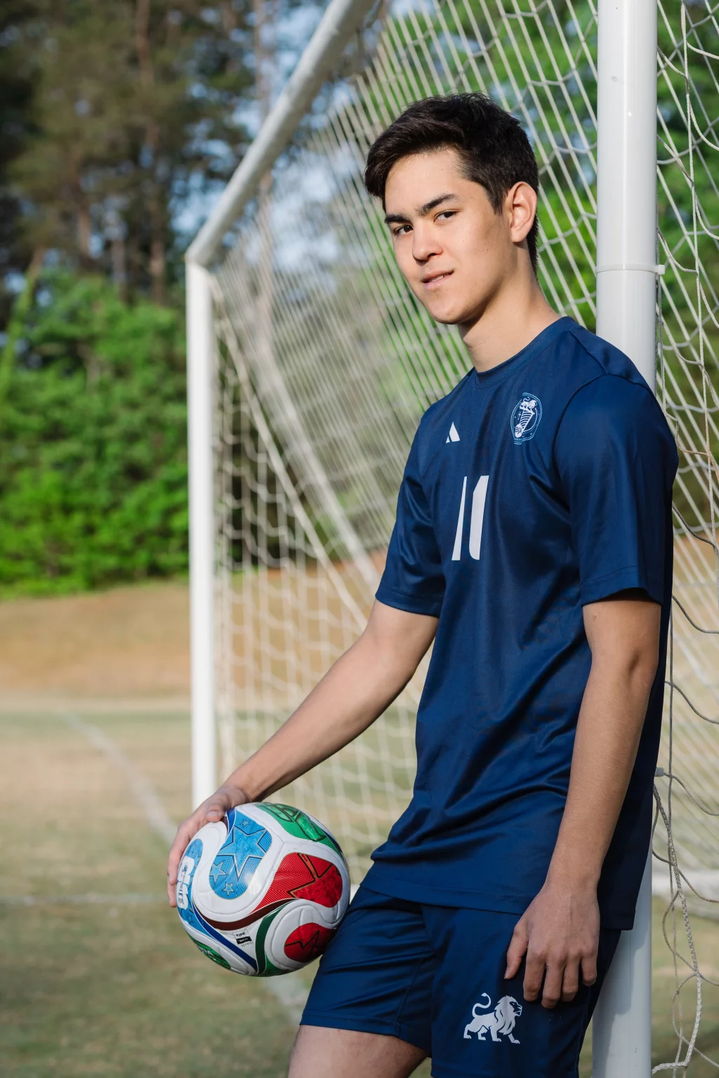 Jared's senior photos taken at Furman University: Young soccer player in a blue uniform with the number 11, leaning against a goalpost and holding a colorful soccer ball on a grassy field.
