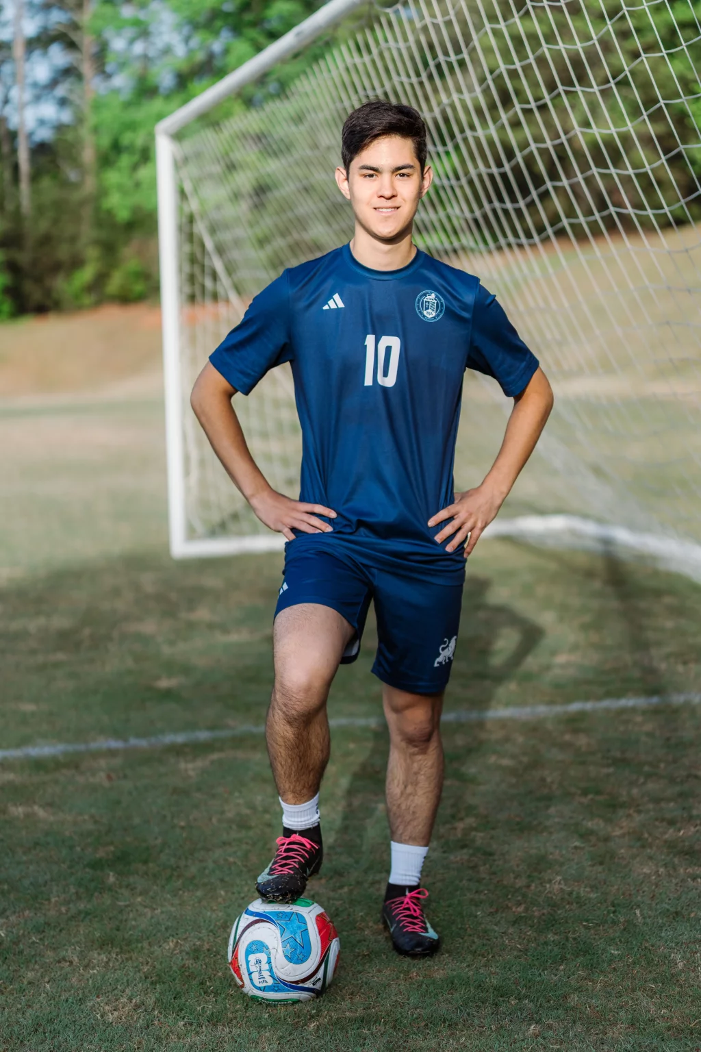 Jared's senior photos taken at Furman University: A soccer player in a blue uniform with the number 10 stands on a field in front of a goal, resting one foot on a soccer ball.