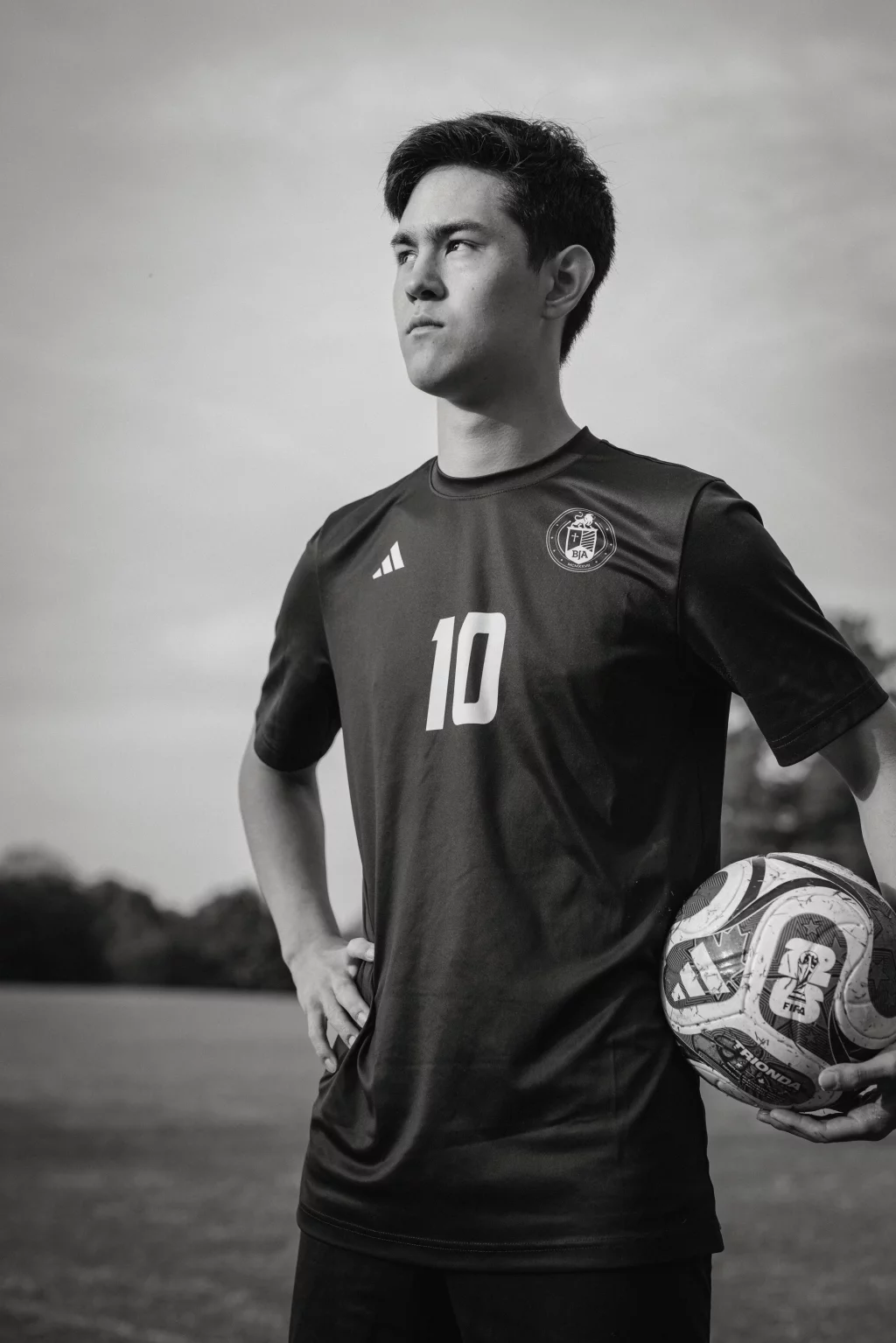 Jared's senior photos taken at Furman University: Black and white photo of a young male soccer player standing outdoors, wearing a jersey with the number 10 and holding a soccer ball under his arm.