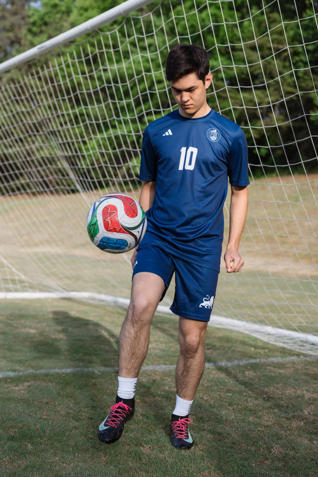 Jared's senior photos taken at Furman University: A soccer player in a blue uniform with the number 10 juggles a soccer ball on a grassy field in front of a goal net.