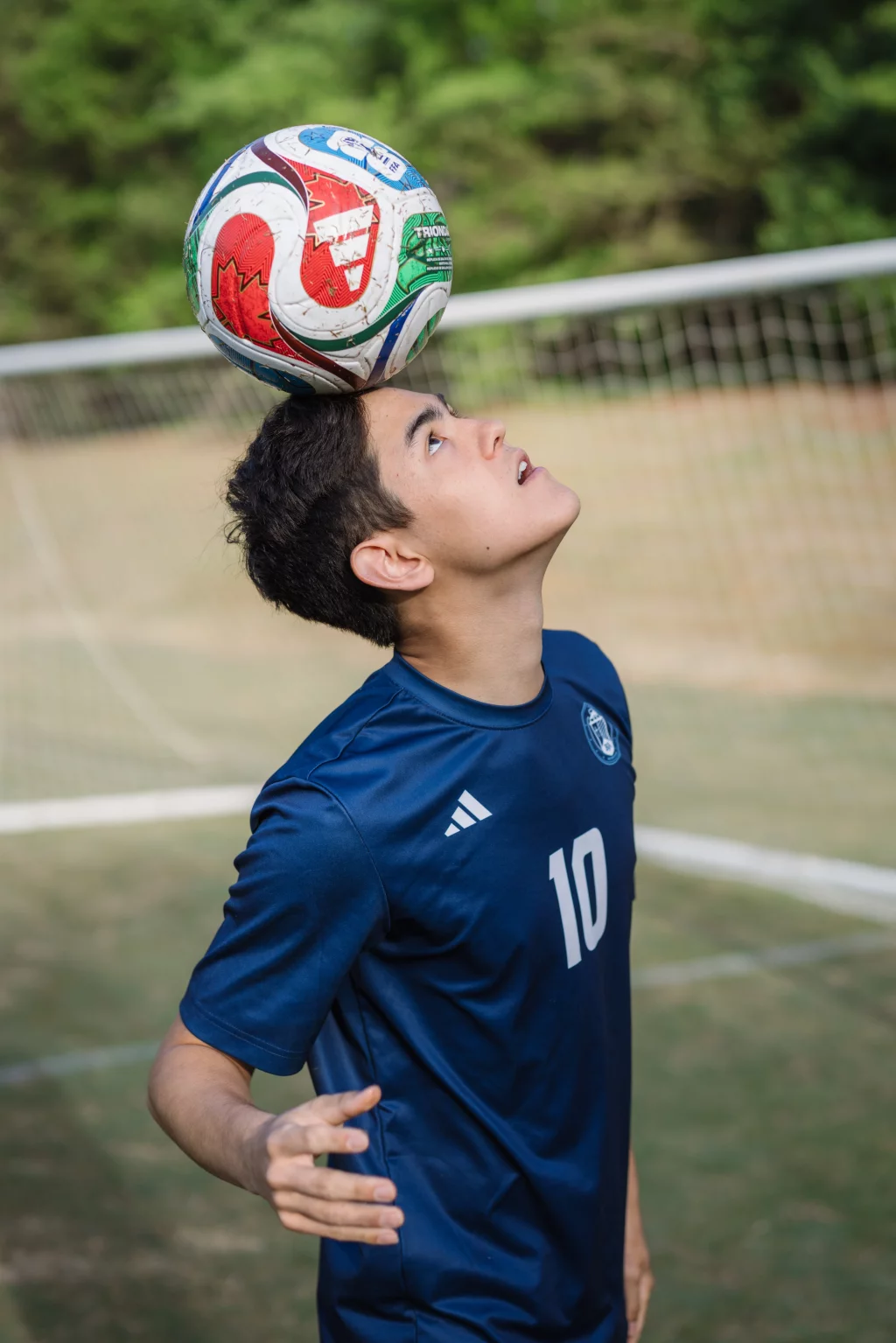 Jared's senior photos taken at Furman University: A soccer player in a blue jersey with the number 10 balances a soccer ball on his forehead on a grassy field, with a goal net in the background.