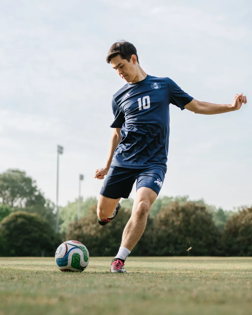 Jared's senior photos taken at Furman University: Soccer player in a blue uniform with number 10 about to kick a soccer ball on a grassy field, with trees and light poles in the background.