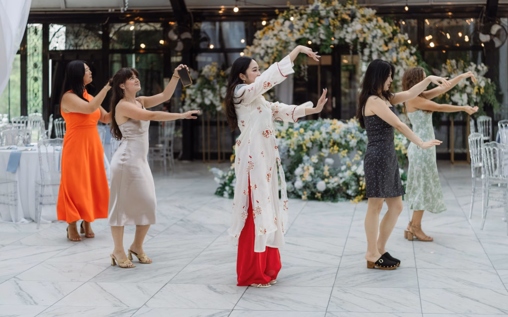 Robbie & Hannah's Wedding @ Edinburgh West, Taylors SC: Five women dance in formation at a wedding reception, surrounded by floral arrangements and banquet tables.