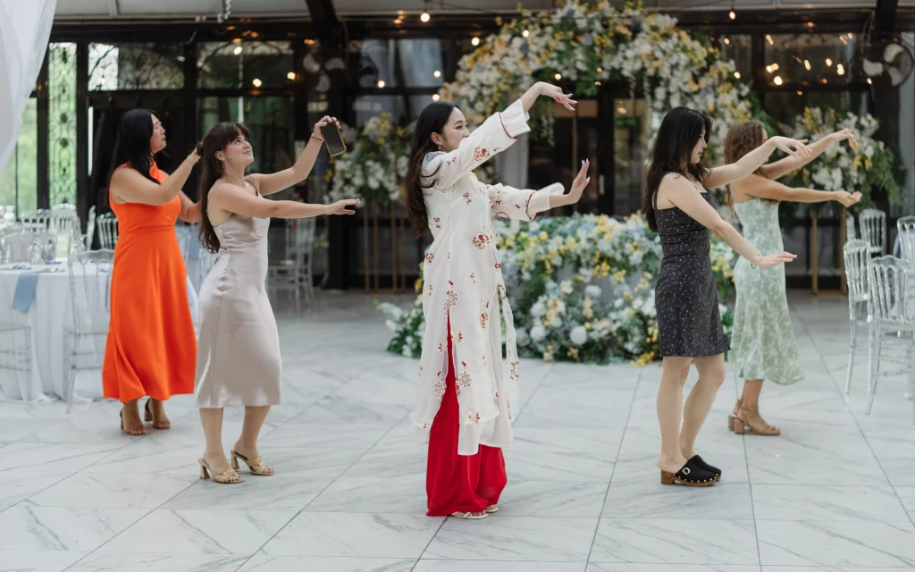 Robbie & Hannah's Wedding @ Edinburgh West, Taylors SC: Five women dance in formation at a wedding reception, surrounded by floral arrangements and banquet tables.