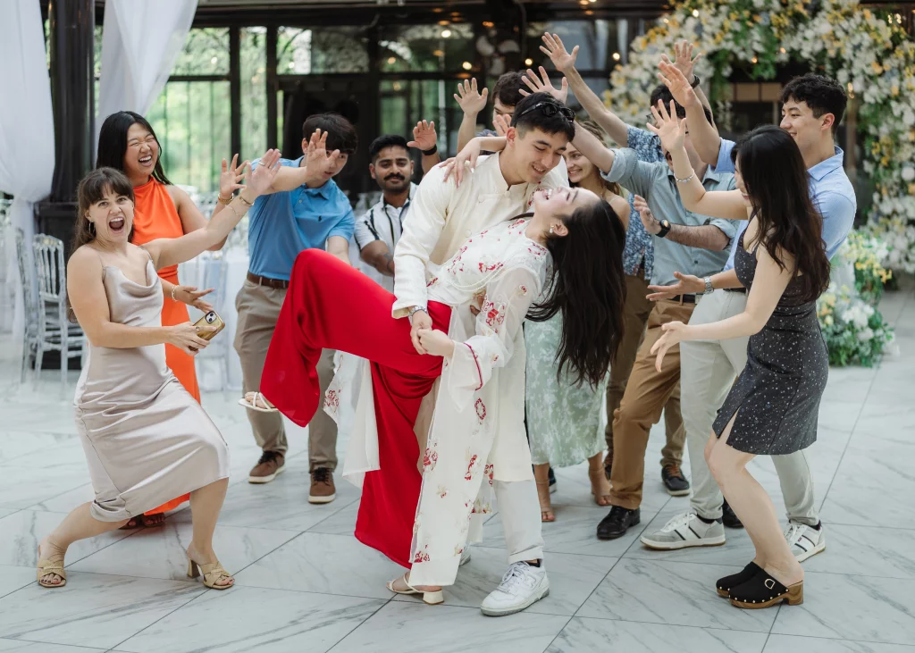 Robbie & Hannah's Wedding @ Edinburgh West, Taylors SC: Wedding guests cheer as a man playfully dips a woman in a bright red-and-white outfit on a marble dance floor.