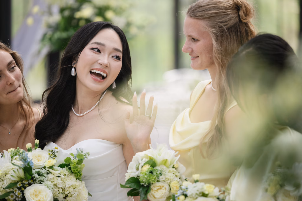 Robbie & Hannah's Wedding @ Edinburgh West, Taylors SC: Bride laughing with two women, surrounded by white and green bouquets at an outdoor wedding.