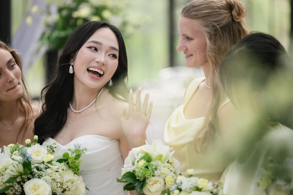 Robbie & Hannah's Wedding @ Edinburgh West, Taylors SC: Bride laughing with two women, surrounded by white and green bouquets at an outdoor wedding.