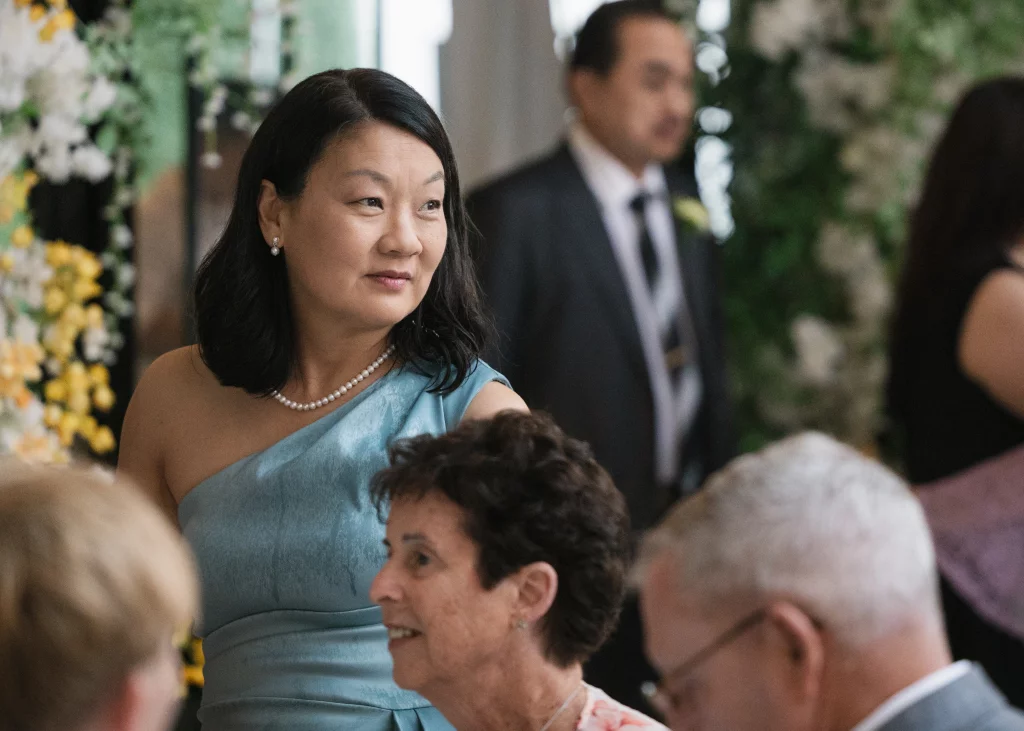 Robbie & Hannah's Wedding @ Edinburgh West, Taylors SC: Wedding guests gathered indoors, including a woman in a light blue dress and pearl necklace.