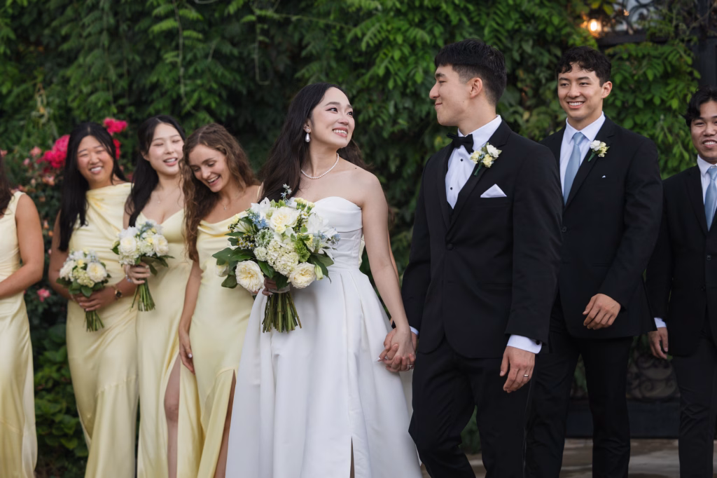 Robbie & Hannah's Wedding @ Edinburgh West, Taylors SC: Bride and groom walk hand in hand with bridesmaids and groomsmen at an outdoor wedding.