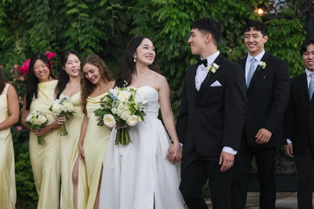 Robbie & Hannah's Wedding @ Edinburgh West, Taylors SC: Bride and groom walk hand in hand with bridesmaids and groomsmen at an outdoor wedding.