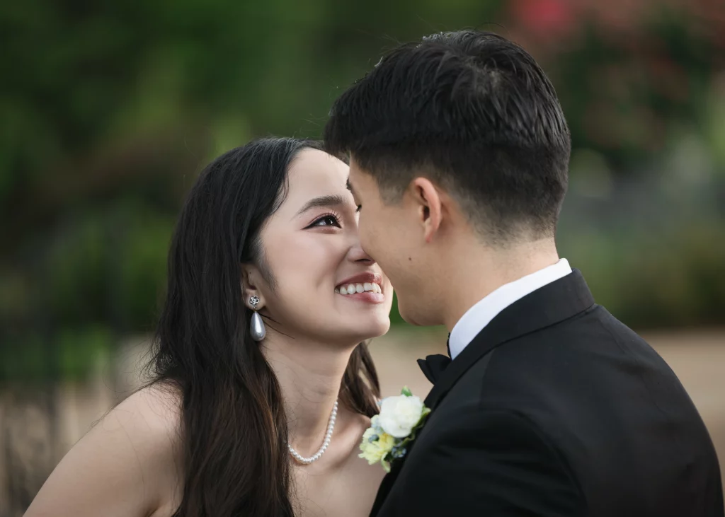Robbie & Hannah's Wedding @ Edinburgh West, Taylors SC: Bride smiling at groom in a black tuxedo during an outdoor wedding portrait.