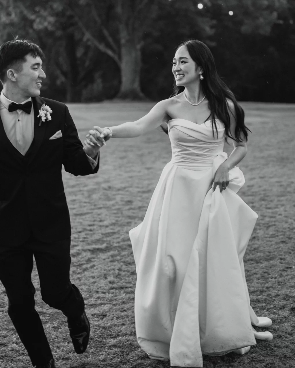 Robbie & Hannah's Wedding @ Edinburgh West, Taylors SC: Bride and groom smiling and holding hands as they walk across a grassy lawn.