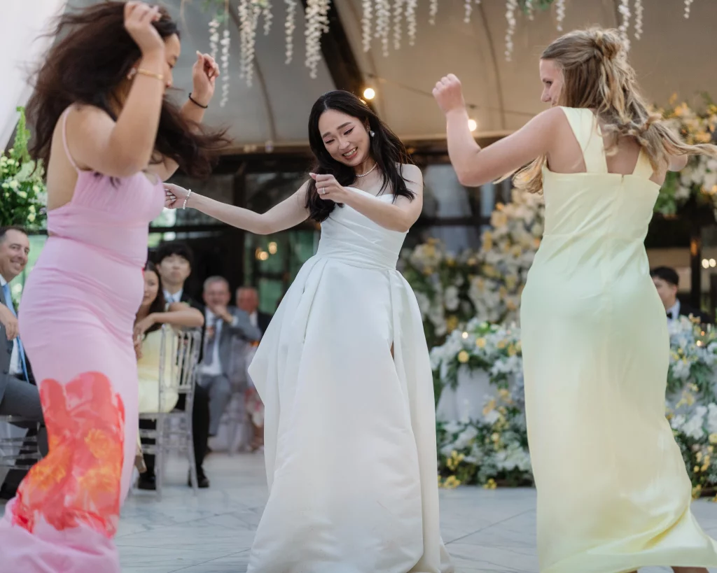 Robbie & Hannah's Wedding @ Edinburgh West, Taylors SC: Bride and two guests dance together at a wedding reception surrounded by floral decorations.
