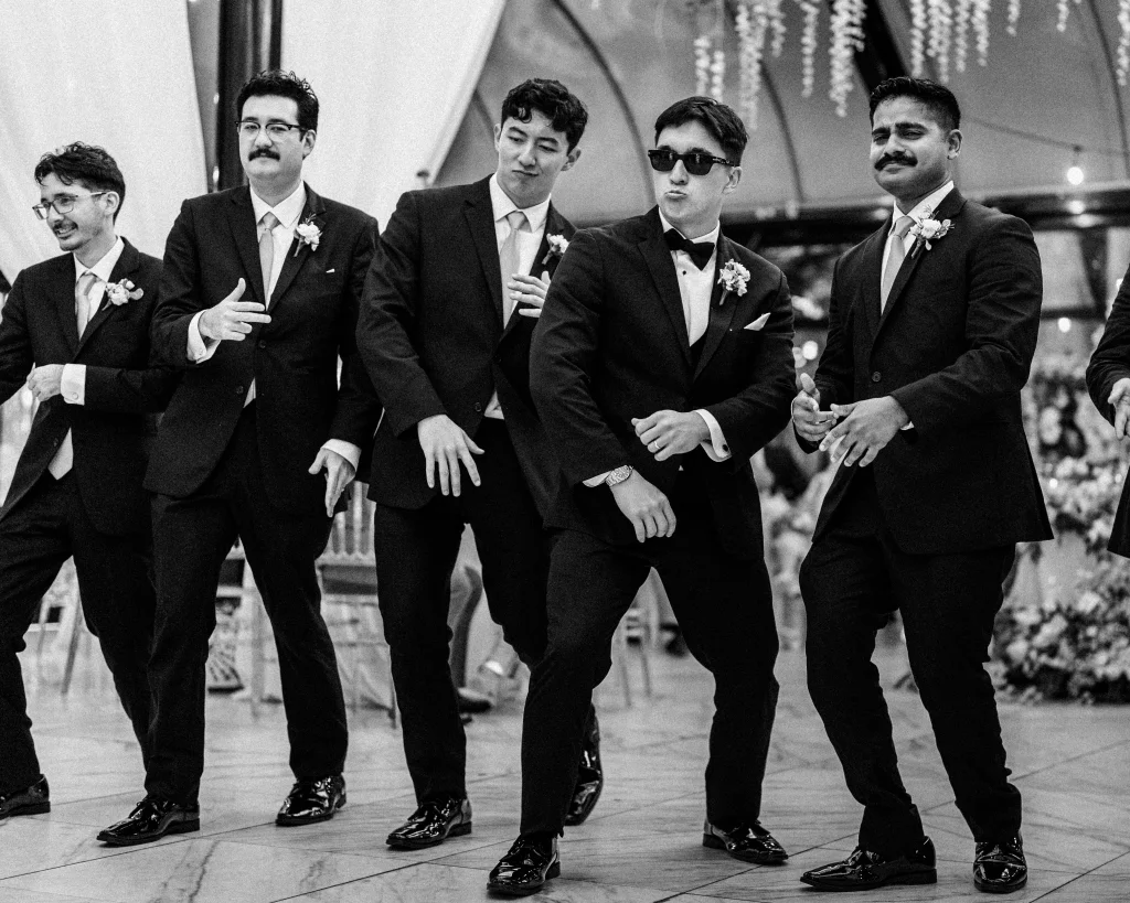 Robbie & Hannah's Wedding @ Edinburgh West, Taylors SC: Five groomsmen in suits and boutonnieres pose playfully at a wedding reception.