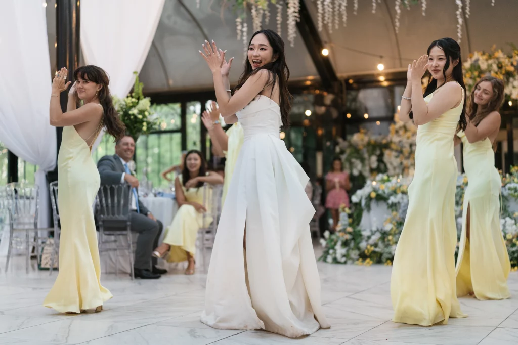 Robbie & Hannah's Wedding @ Edinburgh West, Taylors SC: Bride and bridesmaids dance during a wedding reception, surrounded by floral decorations and seated guests.