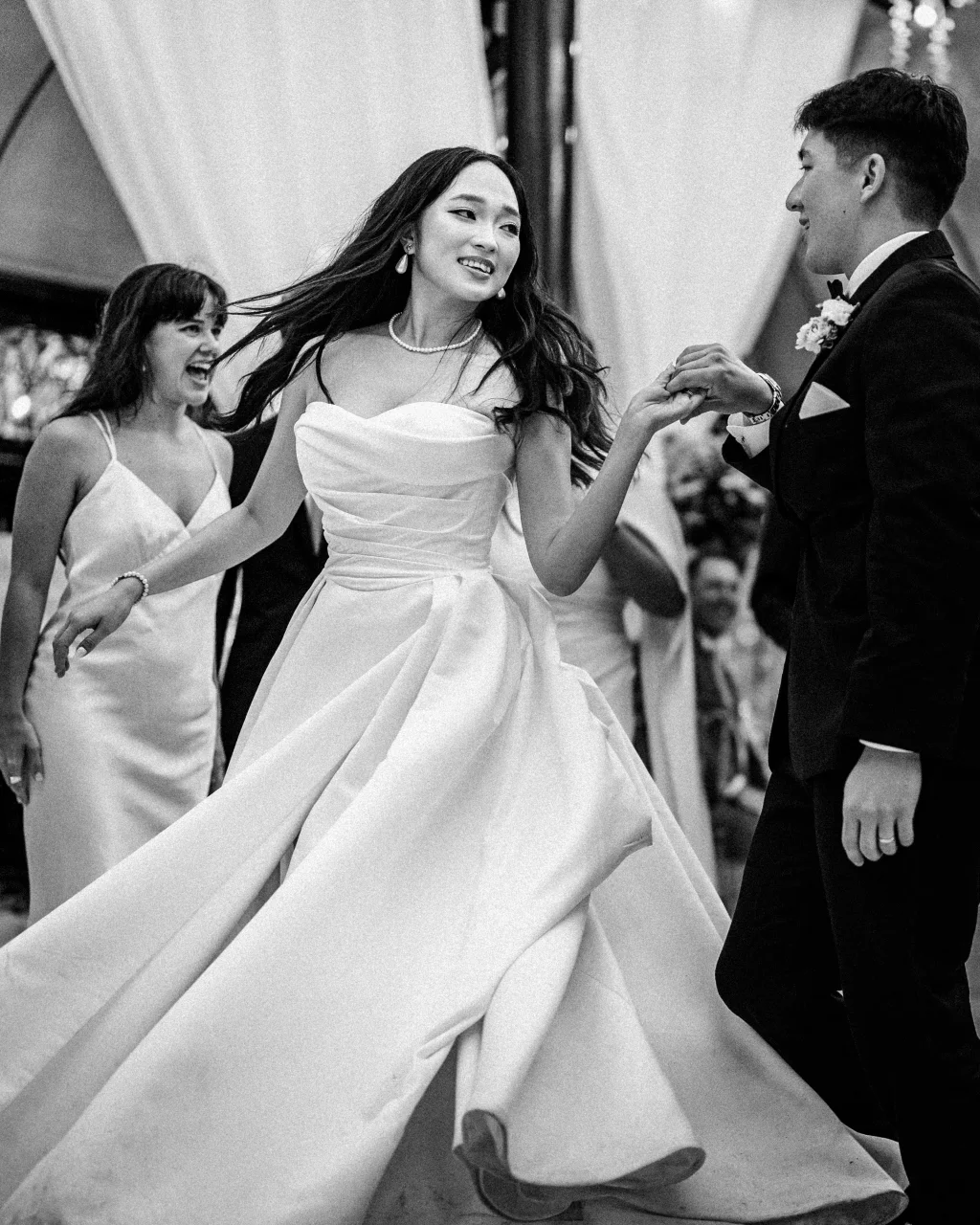 Robbie & Hannah's Wedding @ Edinburgh West, Taylors SC: Bride dancing with groom in a tuxedo as a bridesmaid laughs behind them.