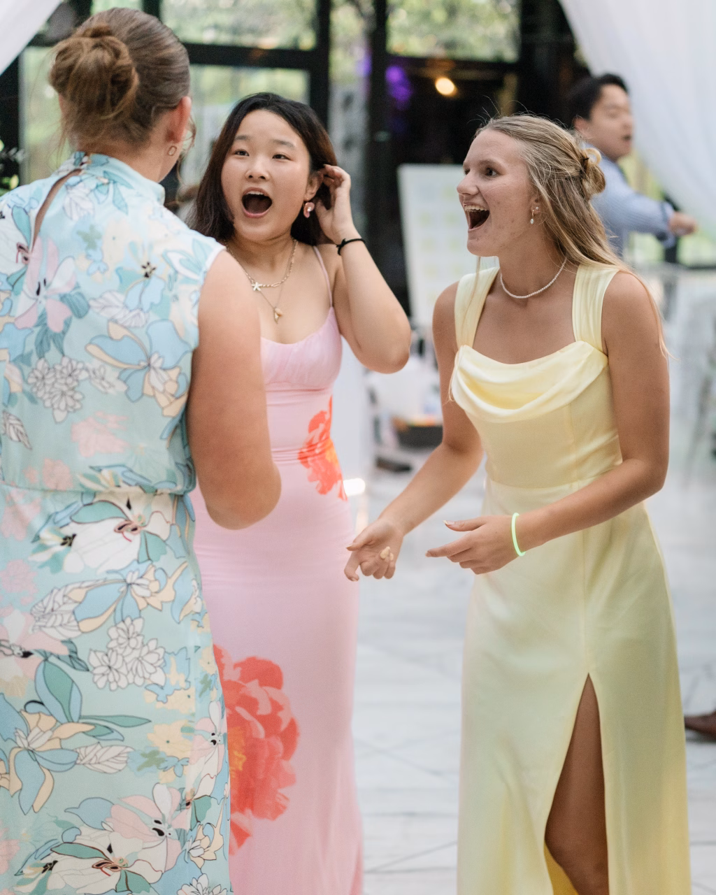 Robbie & Hannah's Wedding @ Edinburgh West, Taylors SC: Three wedding guests in colorful dresses react excitedly while conversing indoors.