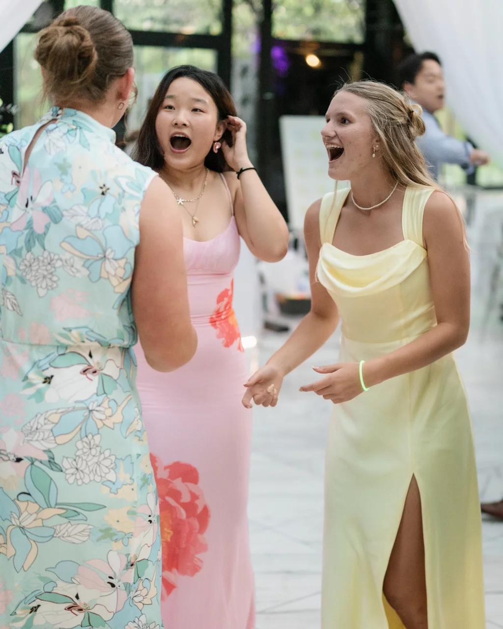 Robbie & Hannah's Wedding @ Edinburgh West, Taylors SC: Three wedding guests in colorful dresses react excitedly while conversing indoors.