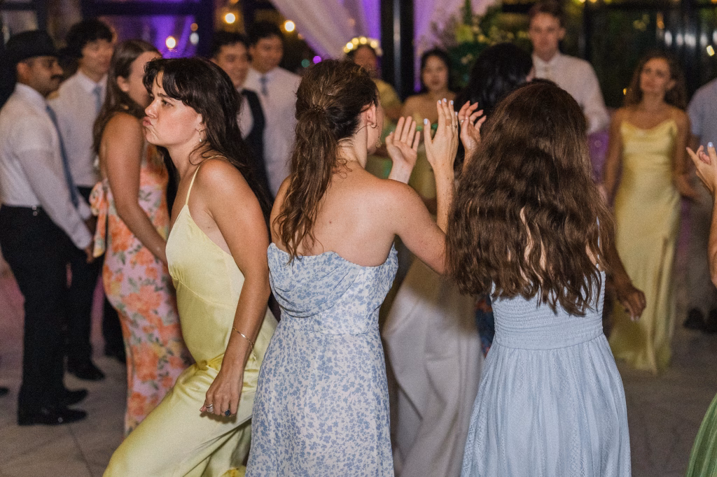 Robbie & Hannah's Wedding @ Edinburgh West, Taylors SC: Wedding guests dance together indoors under purple lighting, with three women in pastel dresses in the foreground.