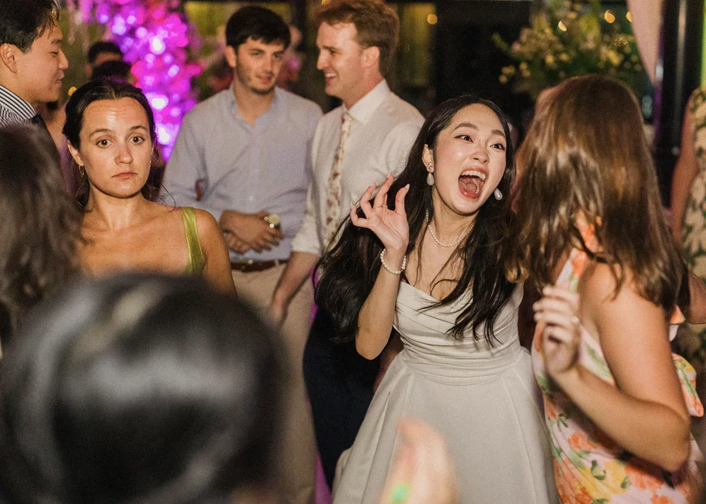 Robbie & Hannah's Wedding @ Edinburgh West, Taylors SC: Guests dance and socialize at a colorful wedding reception, with a smiling woman in a white dress in the foreground.