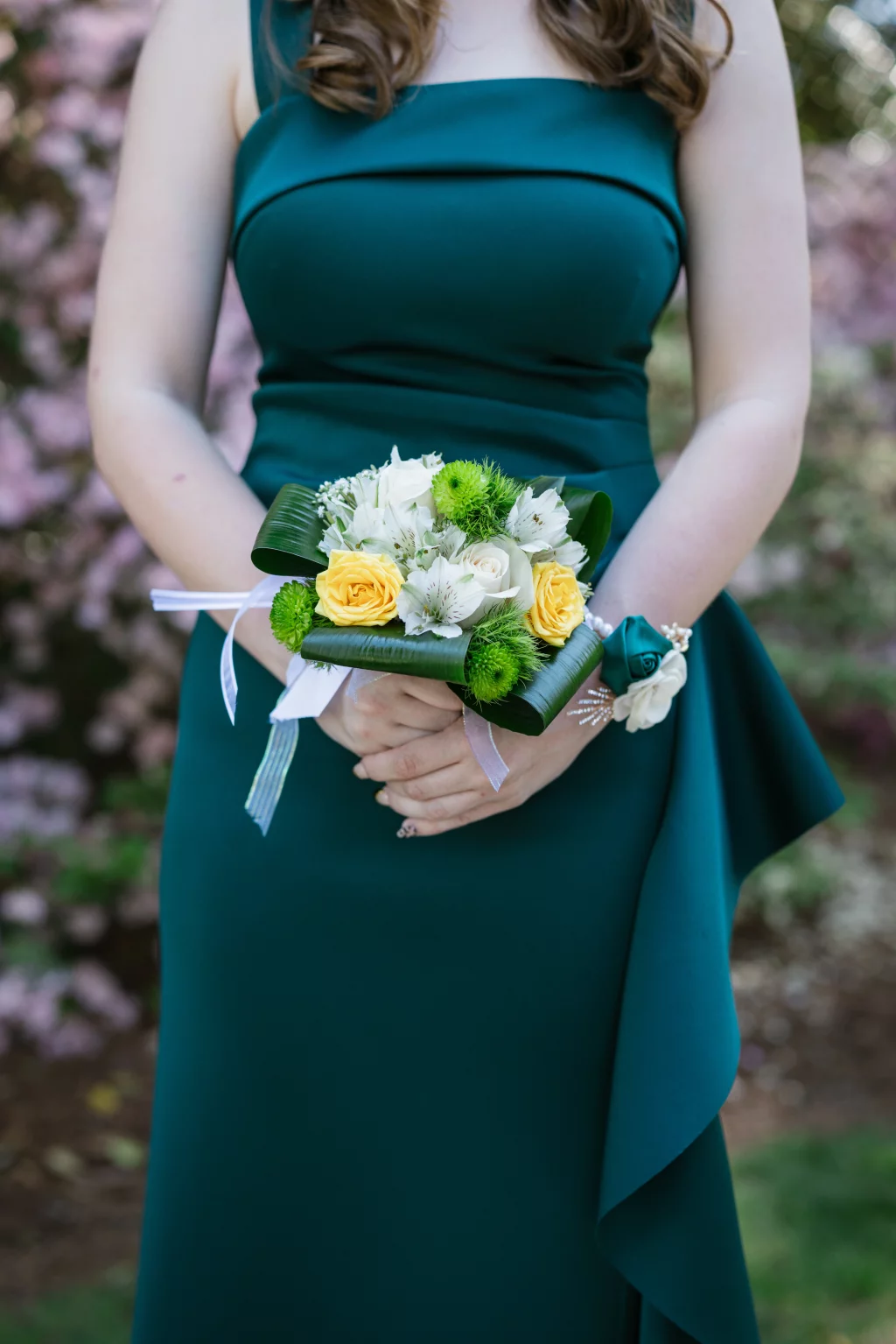 BJA Jr/Sr Banquet Prom at Sue Simpson Park: A person in a dark green dress holding a small bouquet of yellow, white, and green flowers, with a matching corsage on their wrist.