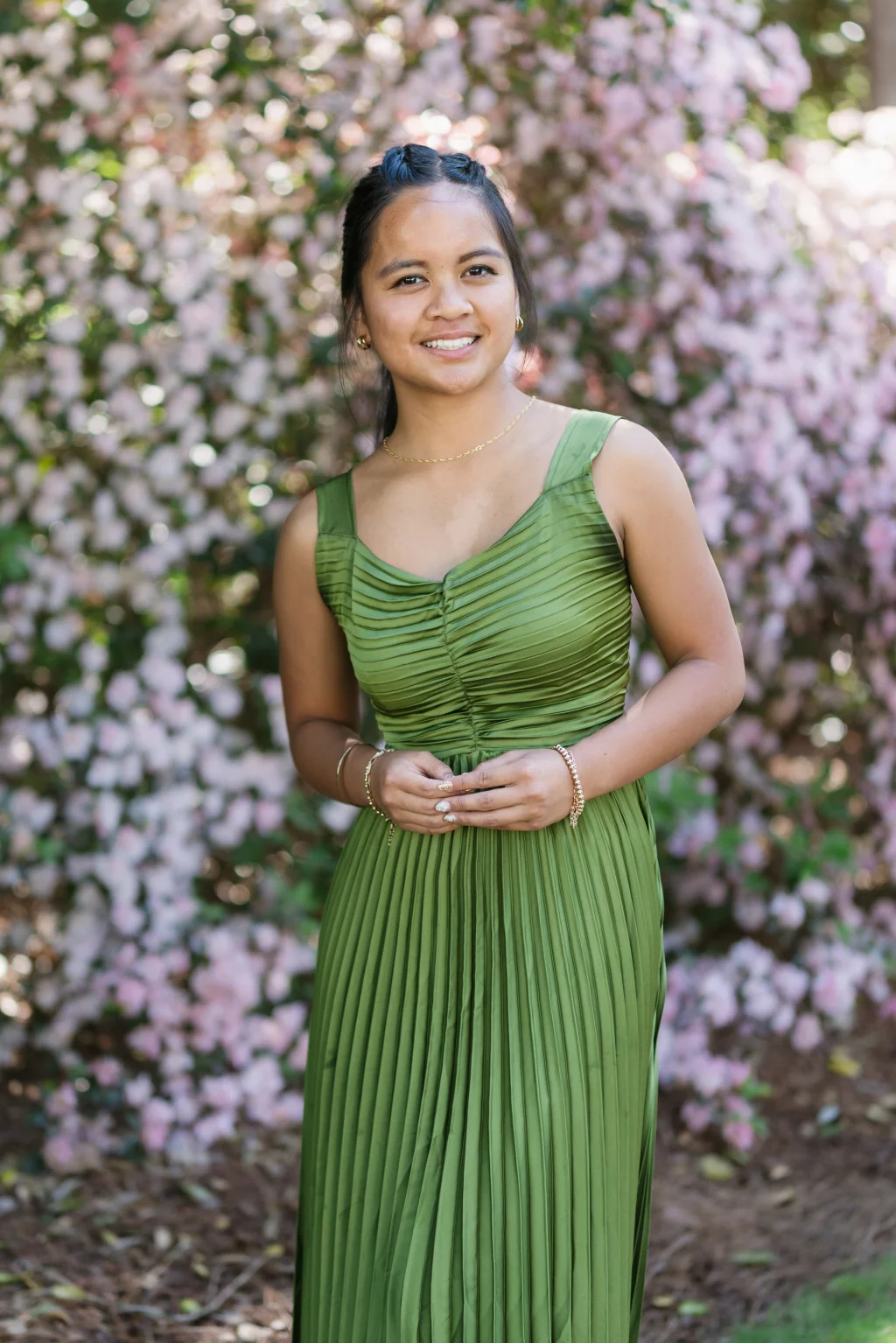 BJA Jr/Sr Banquet Prom at Sue Simpson Park: Woman in a pleated green dress standing outdoors in front of blooming pink flowers, smiling at the camera.