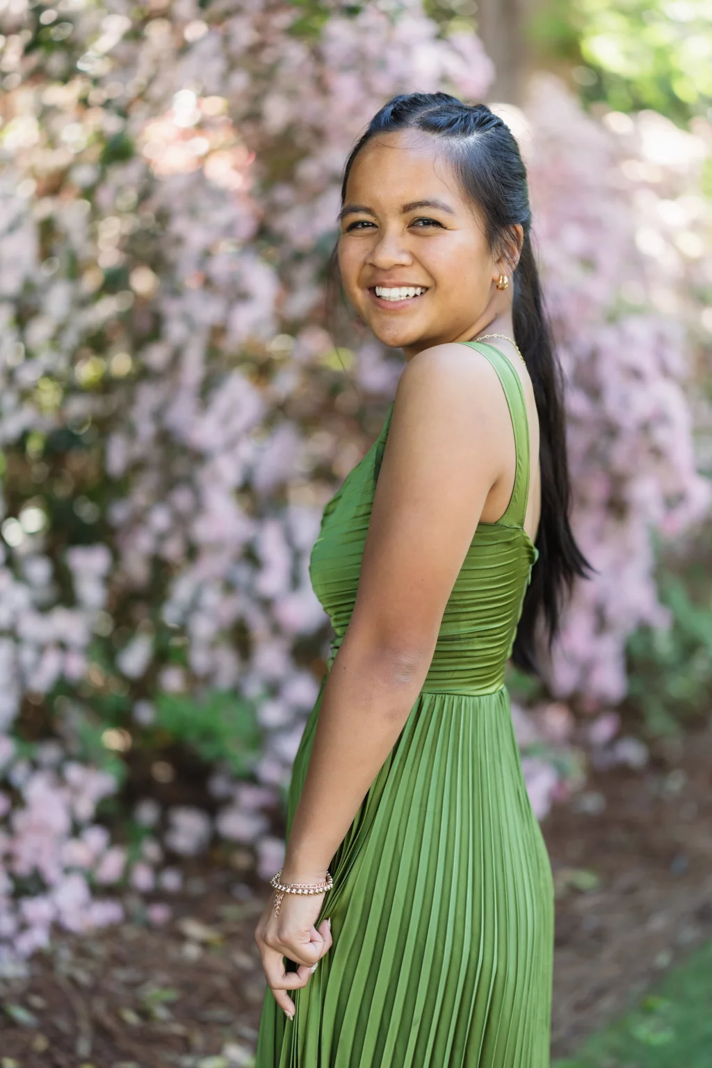 BJA Jr/Sr Banquet Prom at Sue Simpson Park: A young woman in a green pleated dress smiles while standing outdoors in front of blooming pink flowers.