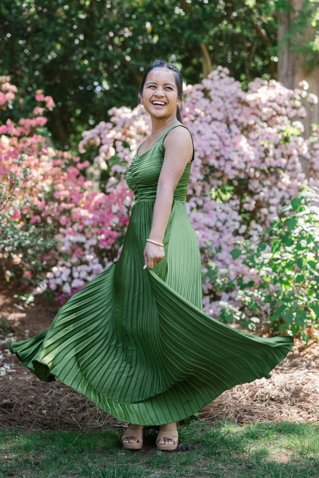 BJA Jr/Sr Banquet Prom at Sue Simpson Park: Woman in a sleeveless green pleated dress twirling and smiling in a garden with blooming pink flowers.