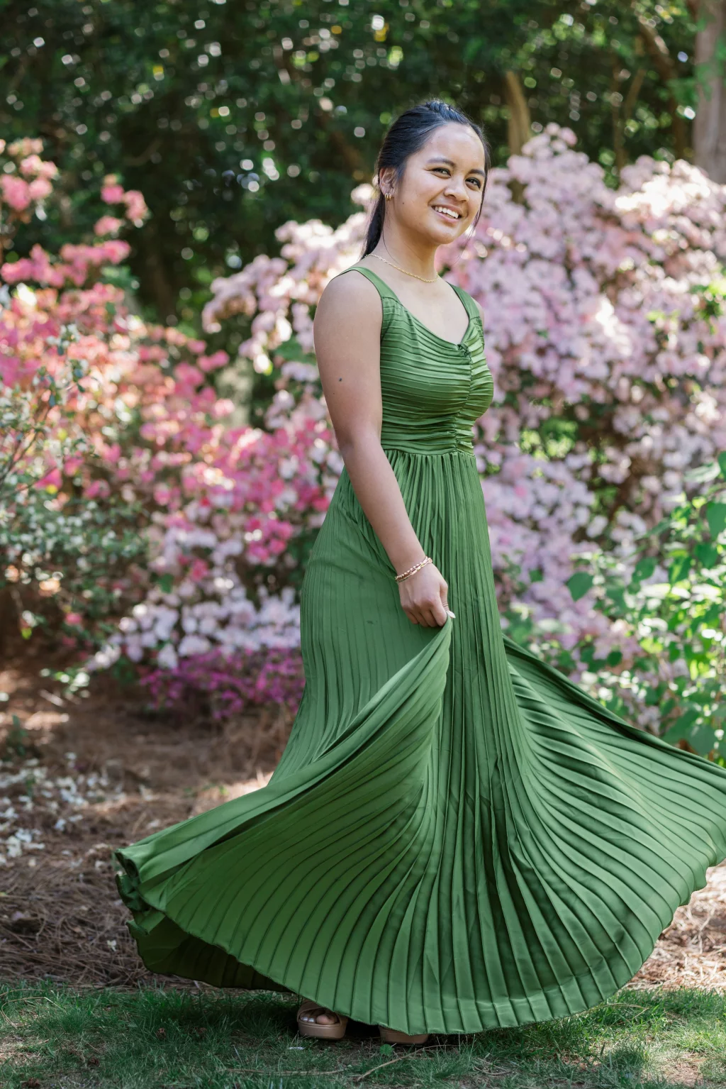 BJA Jr/Sr Banquet Prom at Sue Simpson Park: A young woman in a sleeveless, pleated green dress smiles while standing outdoors in front of blooming pink and white flowers.