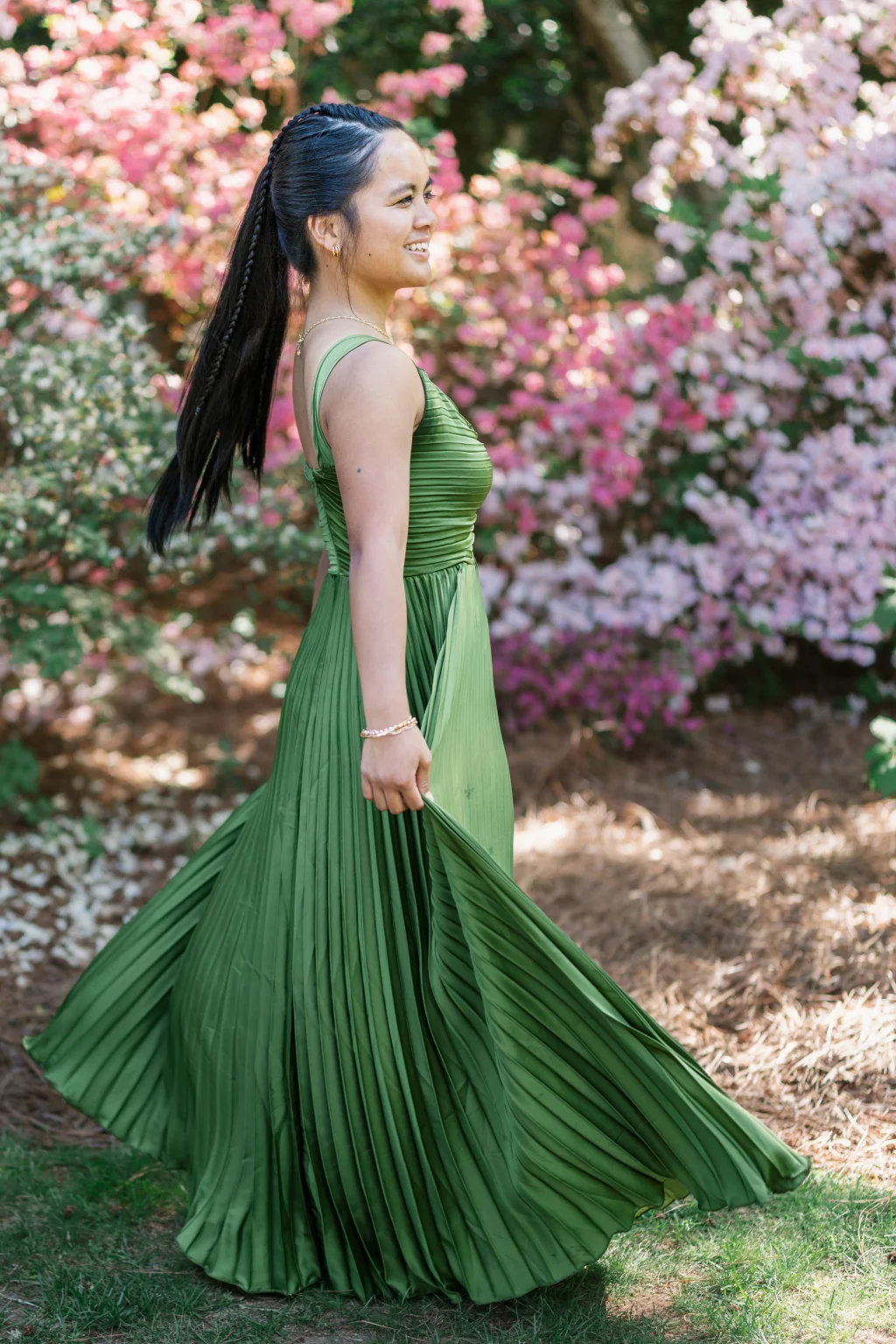 BJA Jr/Sr Banquet Prom at Sue Simpson Park: A young woman in a long, pleated green dress smiles while twirling outdoors, surrounded by blooming pink and white flowers.