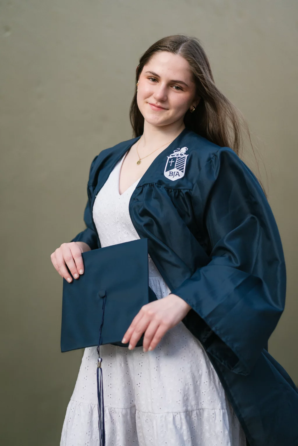 Kellis's senior photos taken Downtown, Greenville, SC: Young woman in a blue graduation gown holding a matching cap, standing against a plain background.
