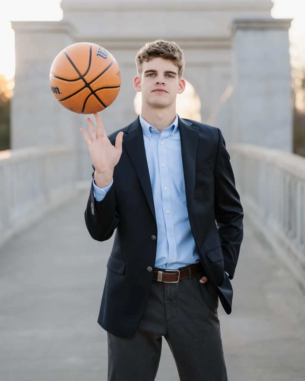 Max's senior photos taken at BridgeWay Station, Simpsonville, SC: Young man in a suit jacket and dress shirt spinning a basketball on his finger while standing on a bridge.