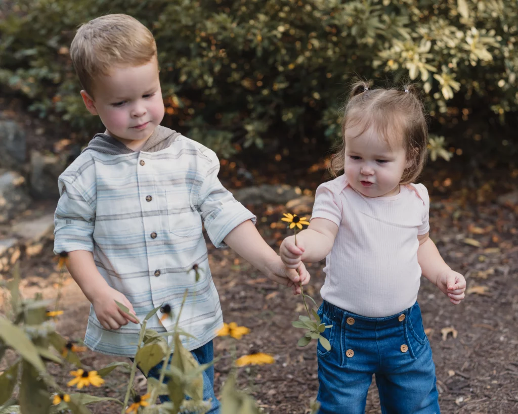 Family session at the Rock Quarry Garden.: Two young children walk through a garden holding hands; the girl holds a yellow flower, while the boy reaches toward flowers in the foreground.