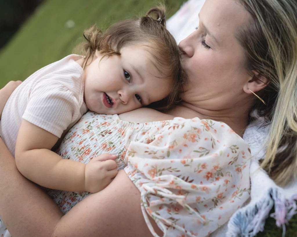 Family session at the Rock Quarry Garden.: A smiling child cuddles against a woman&rsquo;s chest as she kisses the child&rsquo;s head outdoors.