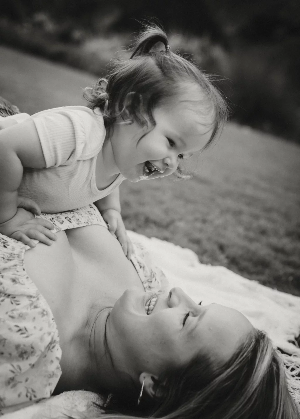 Family session at the Rock Quarry Garden.: Black-and-white photo of a smiling toddler leaning over and laughing with a woman lying on a blanket outdoors.