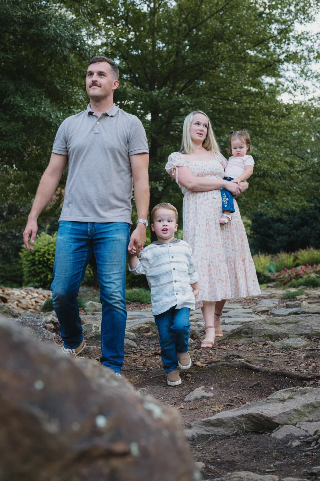 Family session at the Rock Quarry Garden.: A family of four walks along a rocky woodland path: a man holds a young boy&rsquo;s hand while a woman carries a baby.