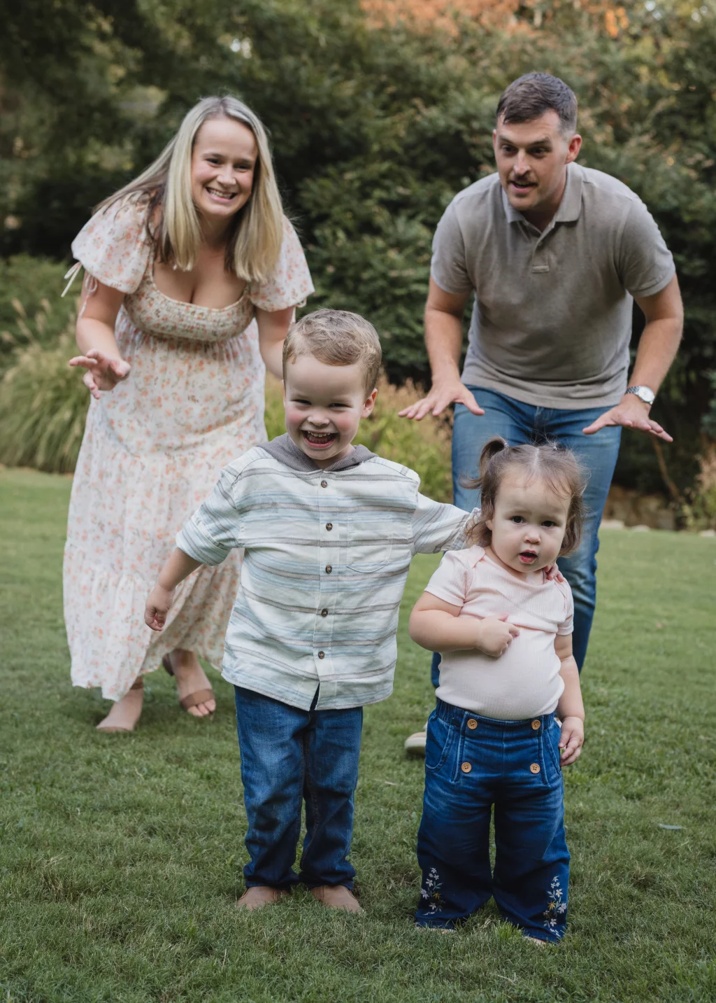 Family session at the Rock Quarry Garden.: A smiling family of four stands on a grassy lawn in a garden, with two children in front and their parents behind them.