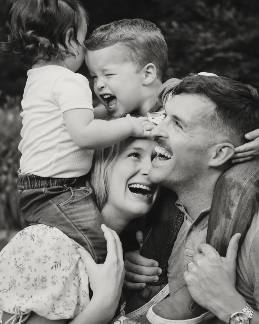 Family session at the Rock Quarry Garden.: Black-and-white portrait of a laughing family outdoors, with two children embracing their smiling parents.