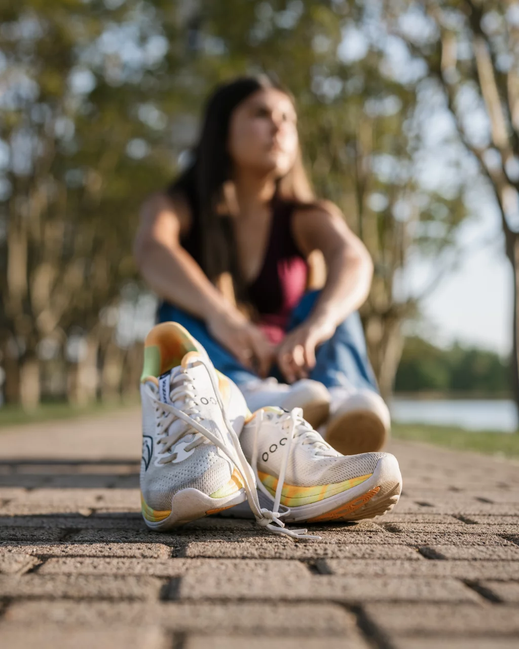 Olivia's senior photos taken at Furman University: A pair of white athletic shoes with yellow accents sits on a paved path in sharp focus, while a person sits cross-legged in the background, blurred, surrounded by trees.
