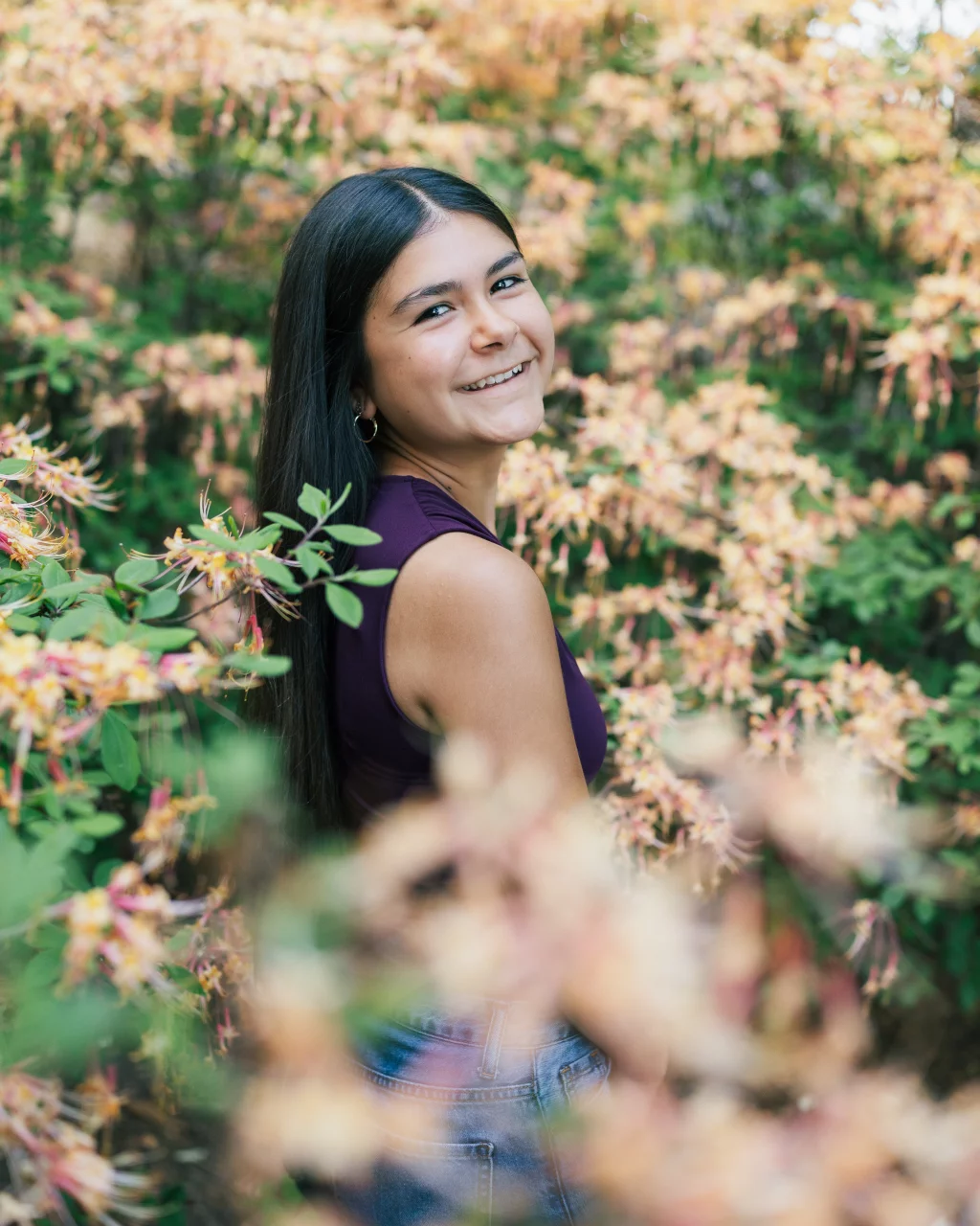 Olivia's senior photos taken at Furman University: Smiling young woman with long dark hair stands outdoors, surrounded by blooming yellow and pink flowers.