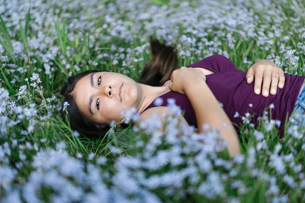 Olivia's senior photos taken at Furman University: A person with long dark hair lies in a field of small, light purple flowers, wearing a purple shirt and looking up at the camera.