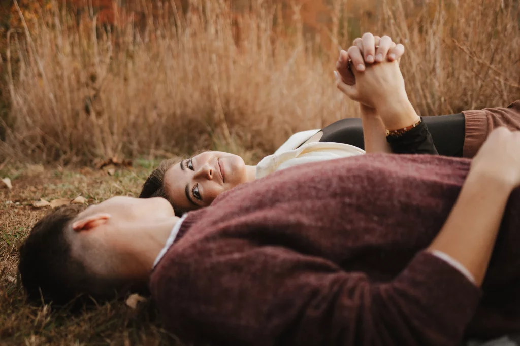 Ethan & Savanah's couple photo session taken at Campbell's Covered Bride, Greenville County: Couple lying on grass in a field, holding hands, with the woman looking at the camera and the man turned away.