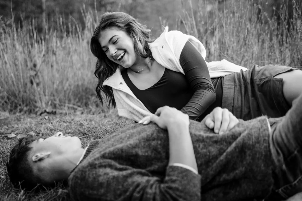 Ethan & Savanah's couple photo session taken at Campbell's Covered Bride, Greenville County: Black and white photo of a young woman laughing while lying on grass and holding hands with a young man lying beside her.