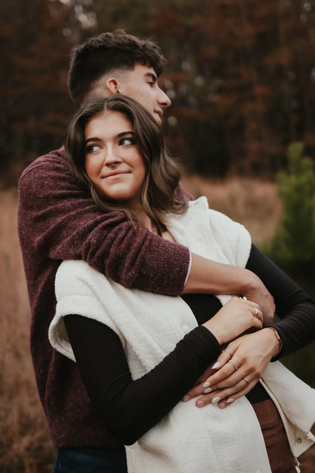 Ethan & Savanah's couple photo session taken at Campbell's Covered Bride, Greenville County: Young couple embracing outdoors in autumn, the woman smiling softly and the man with his eyes closed, surrounded by fall foliage.