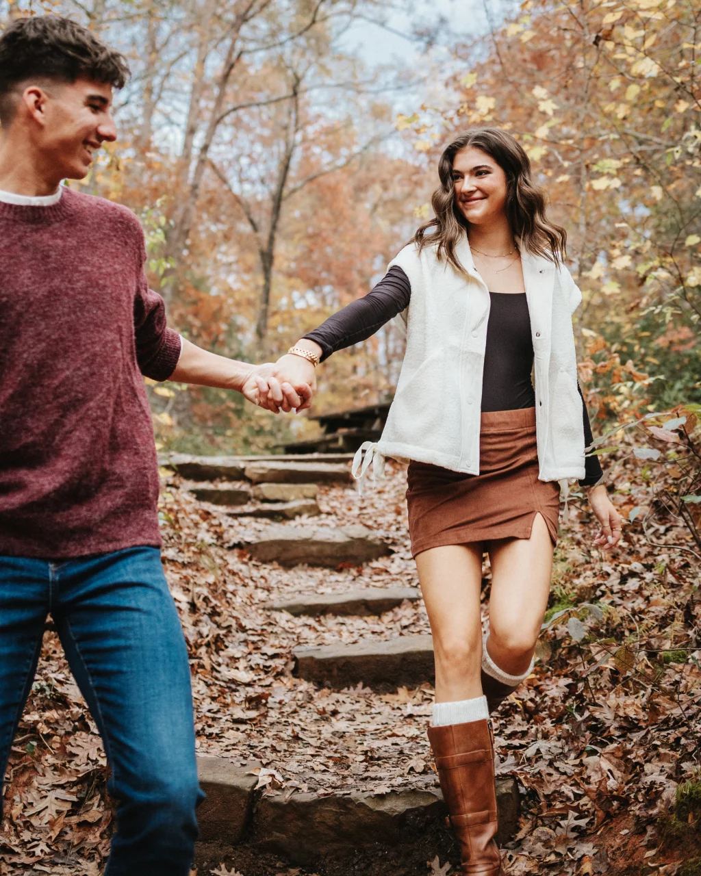 Ethan & Savanah's couple photo session taken at Campbell's Covered Bride, Greenville County: Young couple holding hands walking down leaf-covered outdoor stone steps in autumn forest.