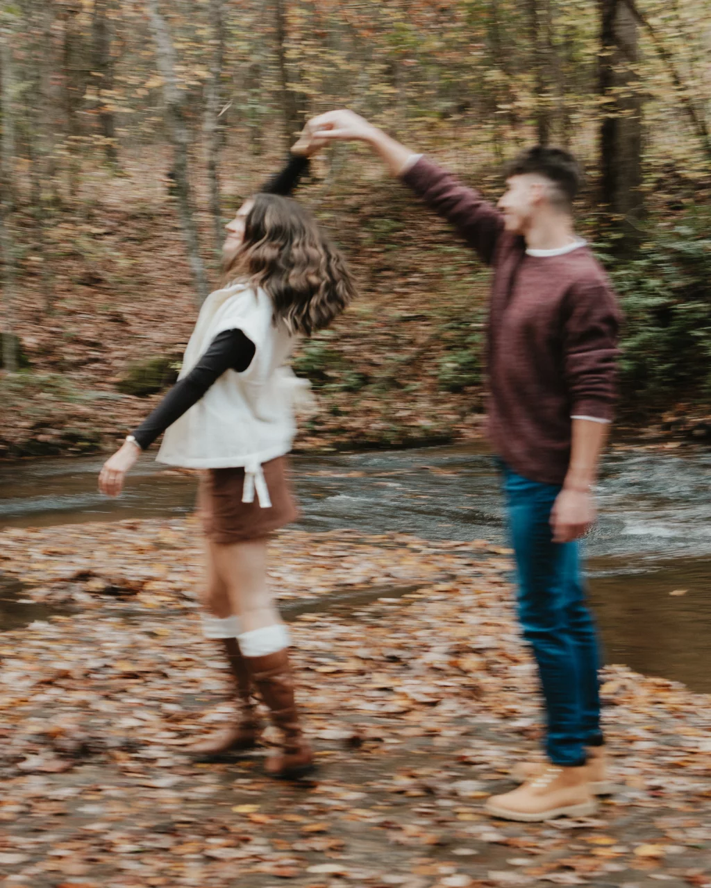 Ethan & Savanah's couple photo session taken at Campbell's Covered Bride, Greenville County: Blurry image of a couple dancing outdoors near a stream, surrounded by autumn leaves and trees.